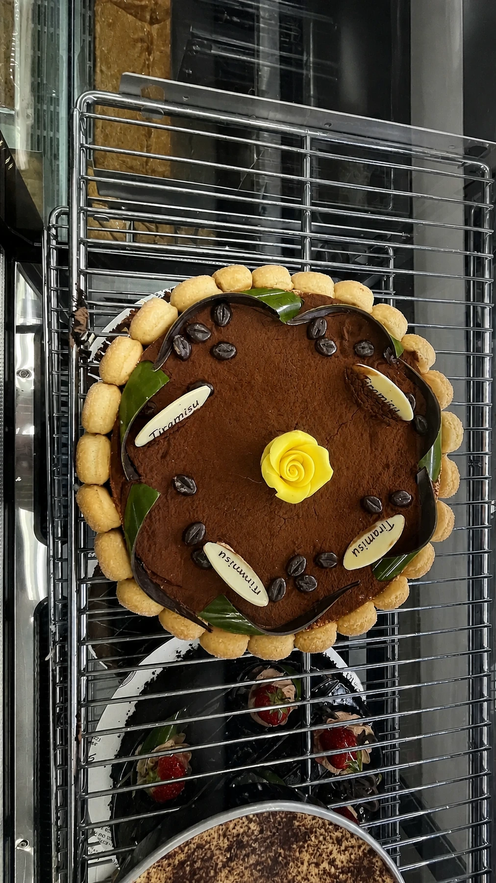 A decorated round tiramisu cake in the chilled case
